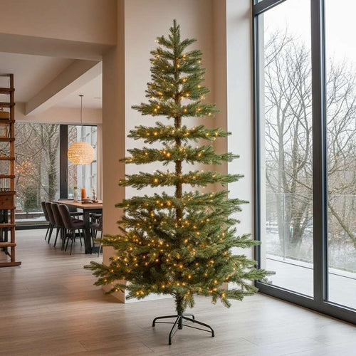 A modern, sparsely branched artificial Christmas tree standing by a tall window in a minimalist home.