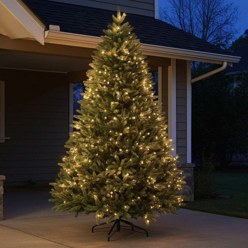A beautifully lit artificial Christmas tree displayed on a home's covered porch at dusk.