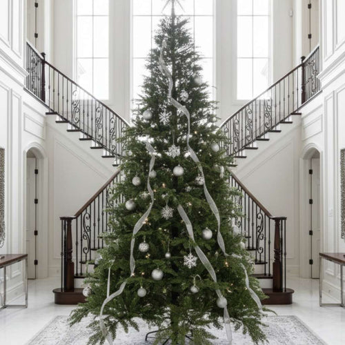 A grand premium Christmas tree decorated in silver, standing in a luxurious foyer with a double staircase.