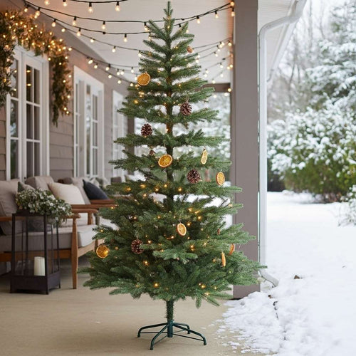 A rustic artificial Christmas tree on a snowy porch, decorated with dried oranges and pinecones.