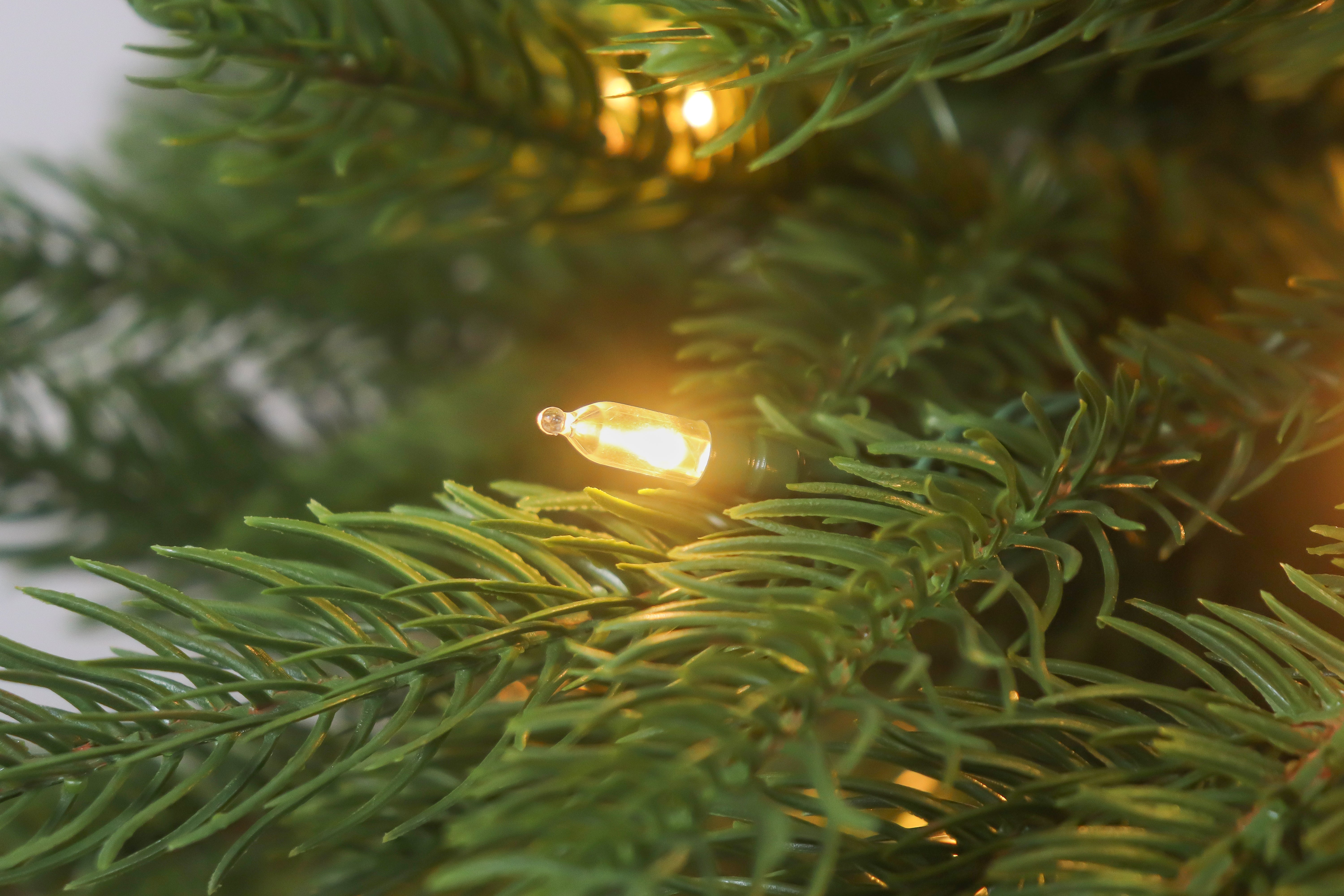 Close-up of a warm white light on a prelit classic christmas tree branch.