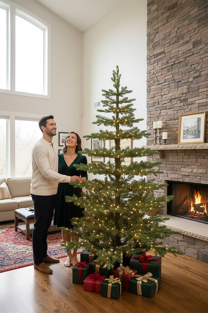 A couple admiring their tall 9-foot pre-lit skinny Christmas tree next to a cozy stone fireplace.
