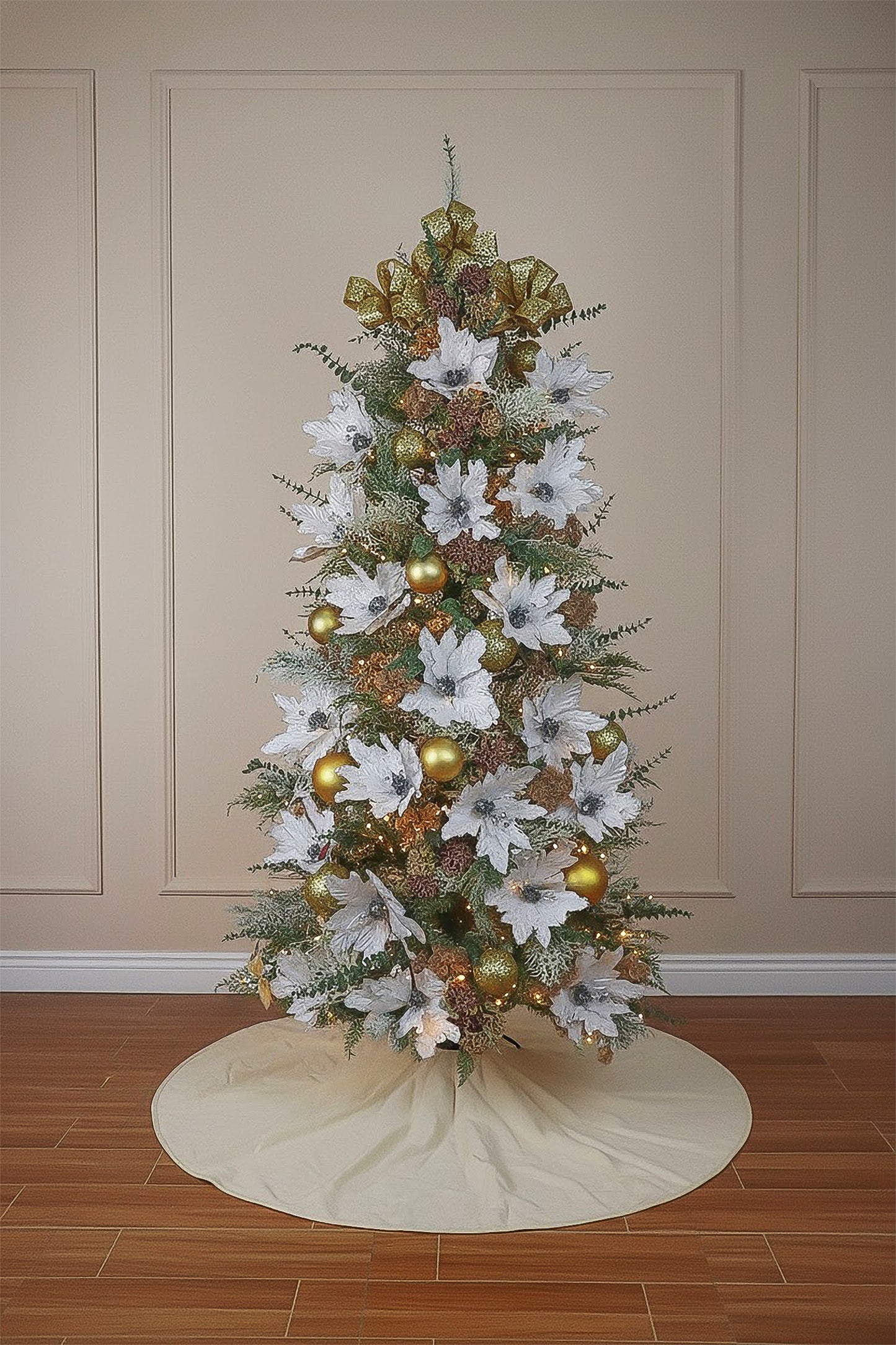 A decorated cypress Christmas tree with large white poinsettias, gold ornaments, and a festive bow topper.