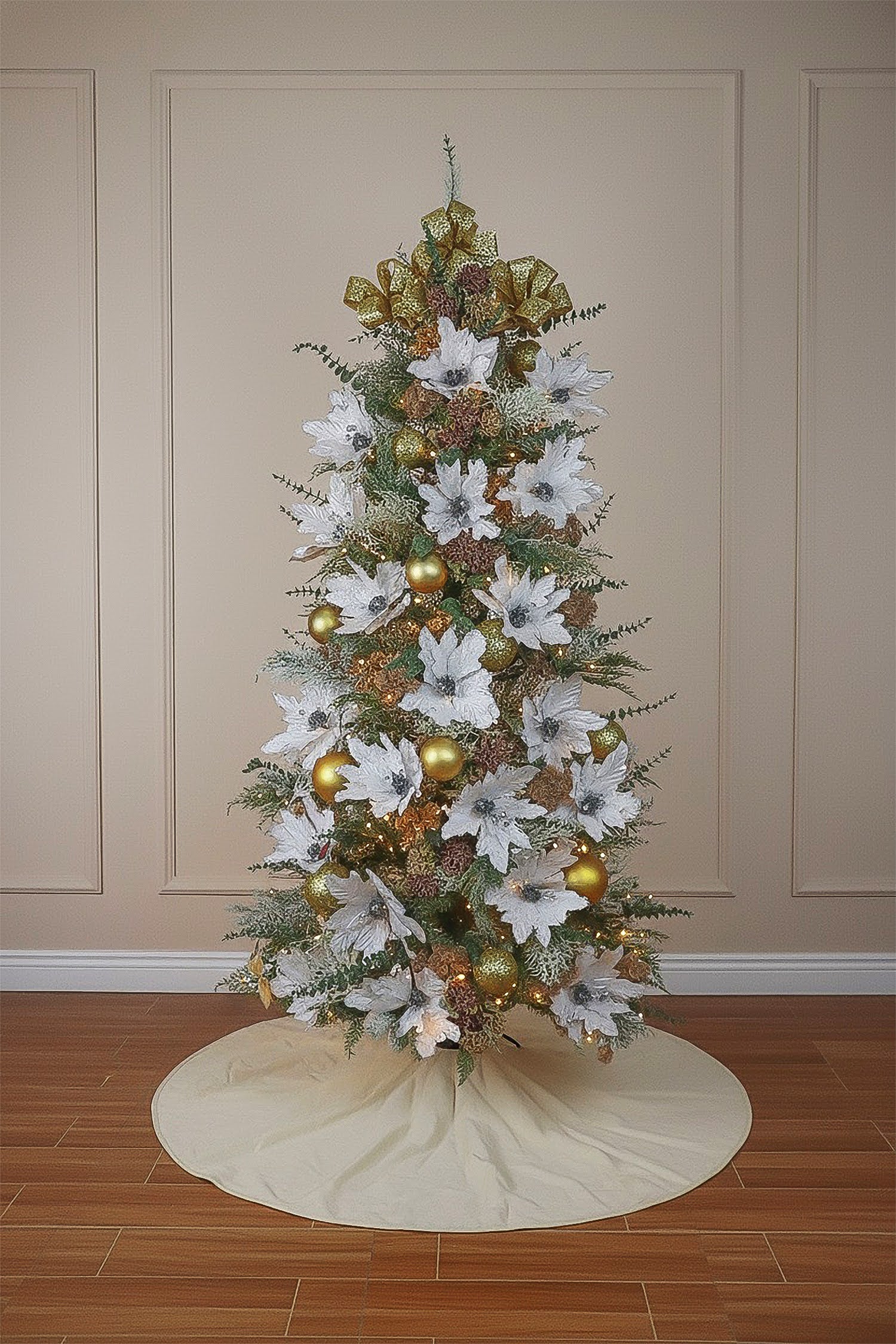 A decorated cypress Christmas tree with large white poinsettias, gold ornaments, and a festive bow topper.