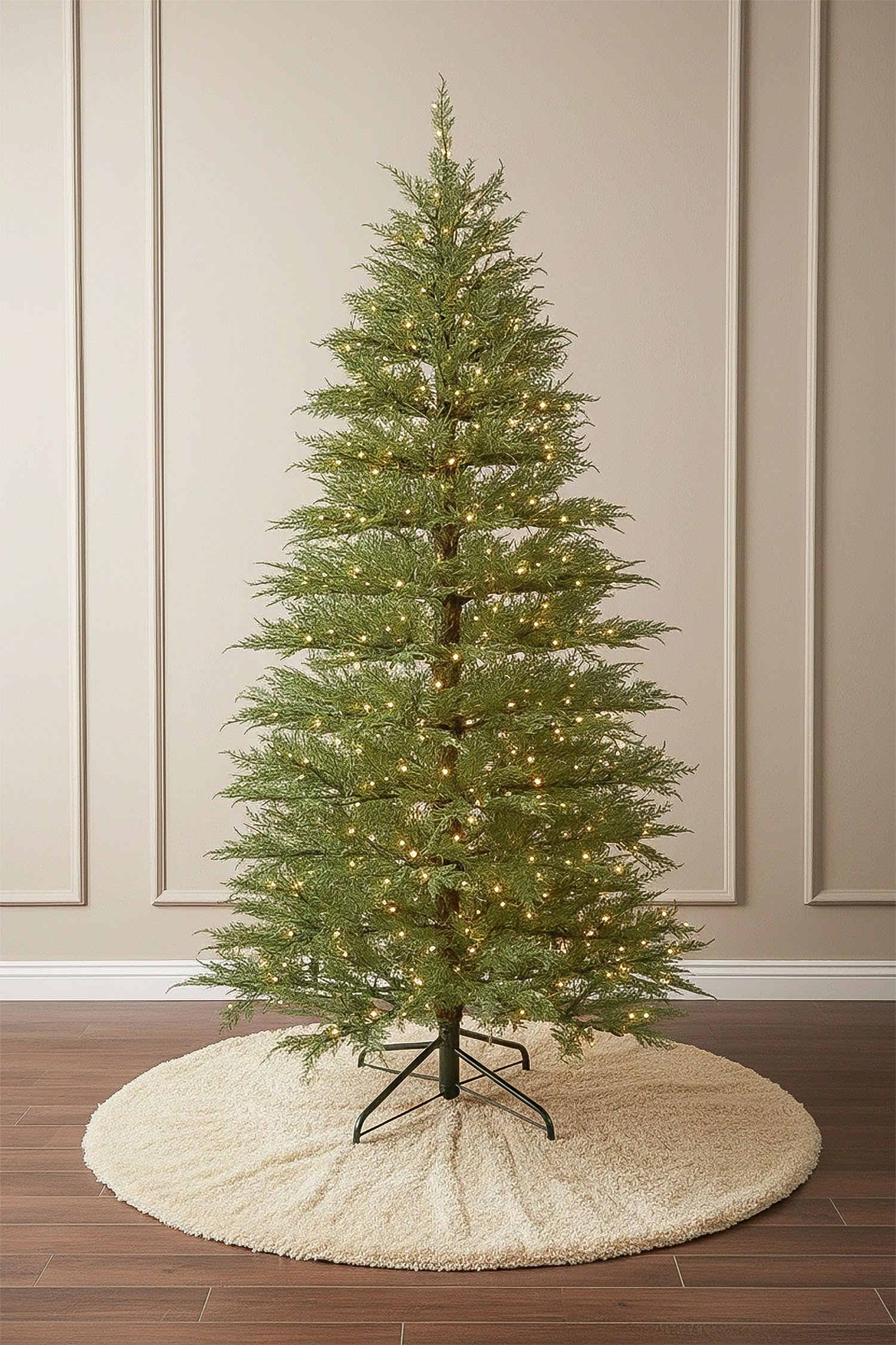 A full-length view of a slender, pre-lit minimalist Christmas tree standing on a dark wood floor.